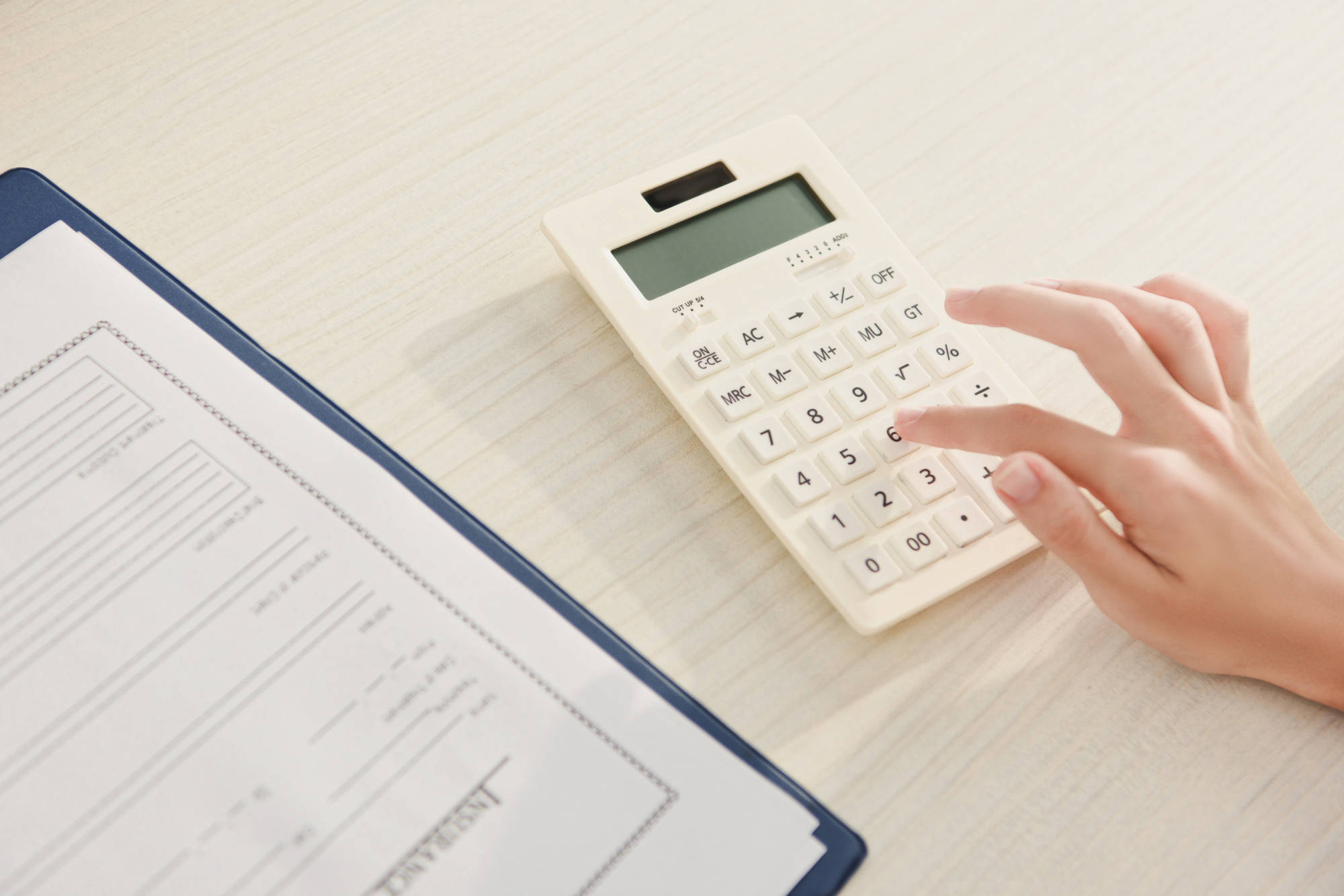 cropped view of woman counting finances on calculator at table with insurance claim form